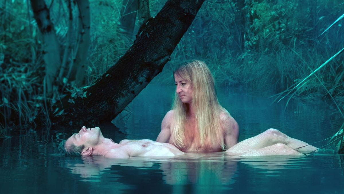 woman in lake holding up man floating in hands