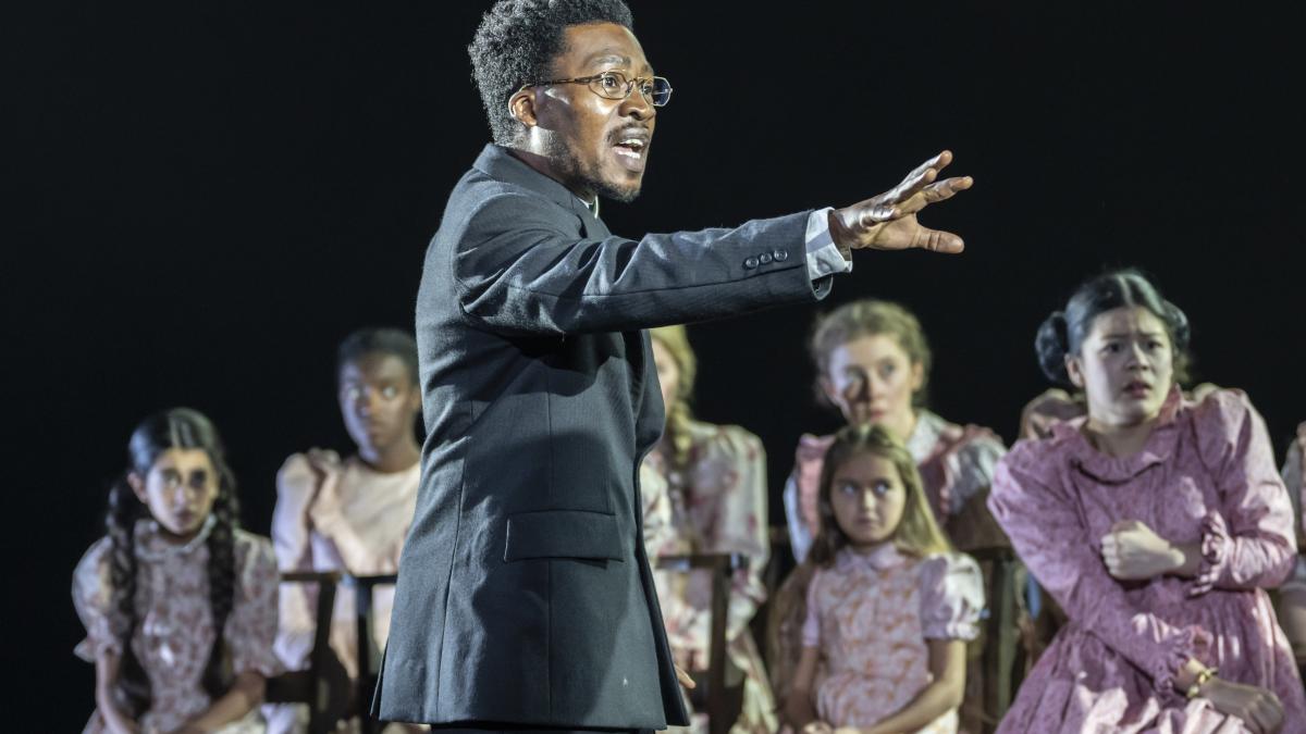 person in uniform standing on stage with outstretched arm