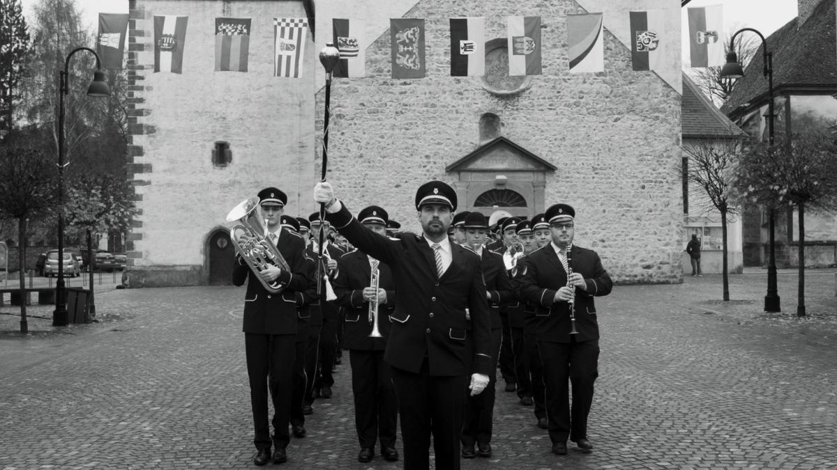 orchestra in uniform marching in front of castle like building with flags hanging