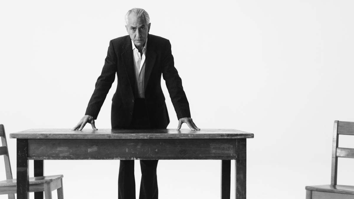black and white photo of man and suit leaning over table with white background