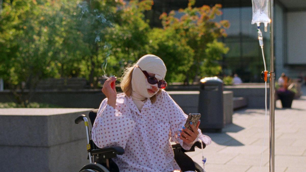 woman with bandaged face sitting in wheelchair outside on cellphone smoking a cigarette
