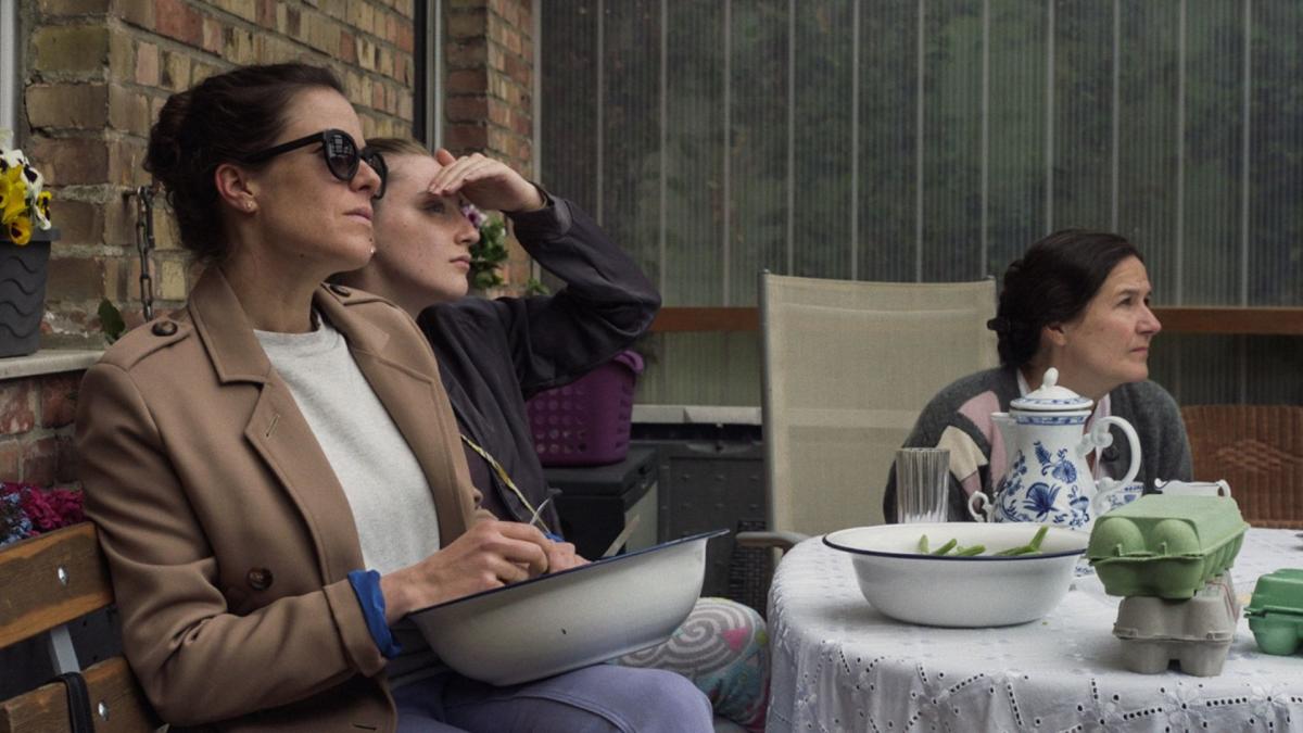 three women sitting outside at table looking at something in distance