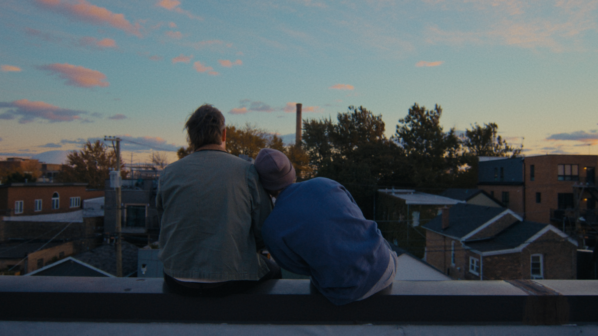 two people sitting on roof looking at sunrise leaning on each other shoulder