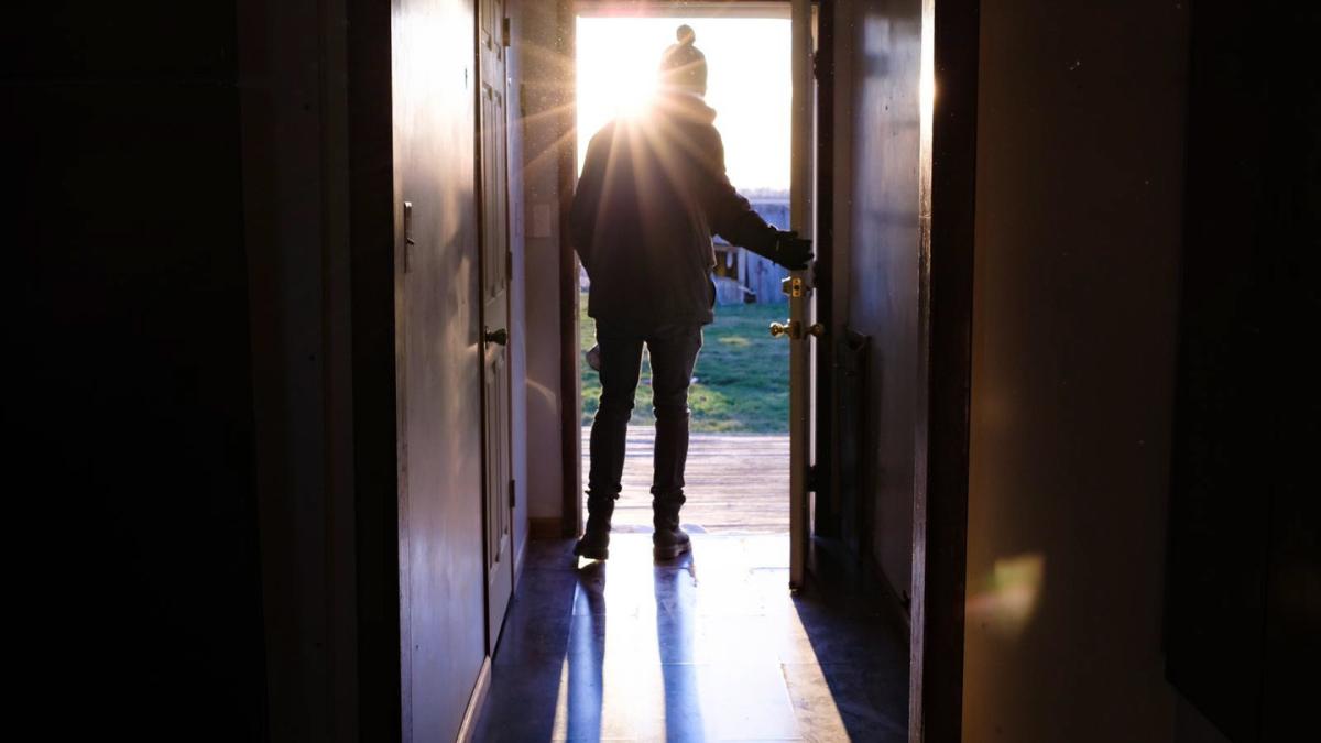 person leaving through doorway of home with sunlight streaming in