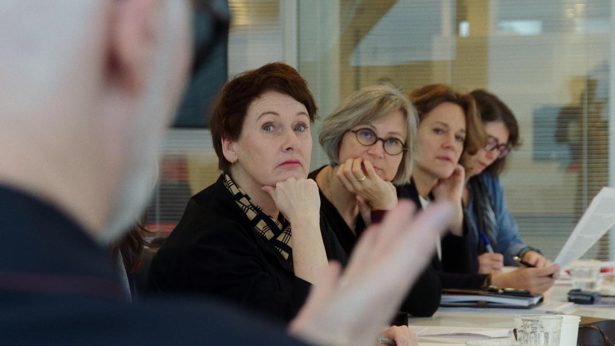 women sitting in conference room turning heads towards man