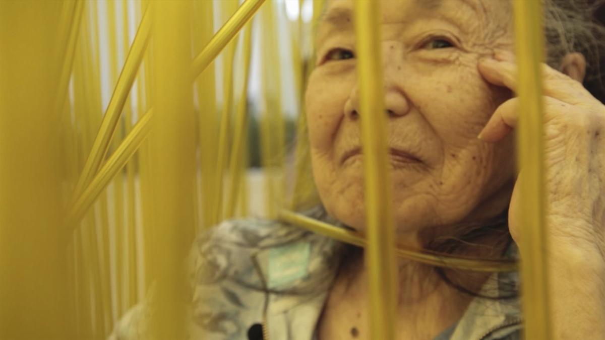 elderly woman smiling at camera through fence