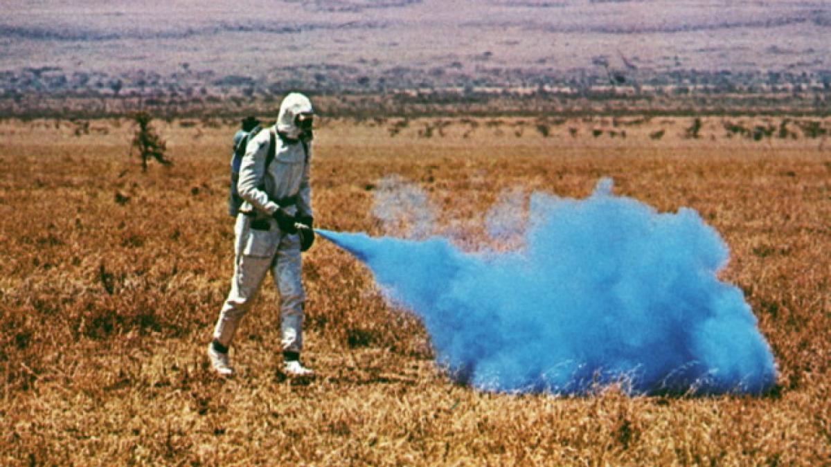man in field wearing spacesuit and blowing blue smoke
