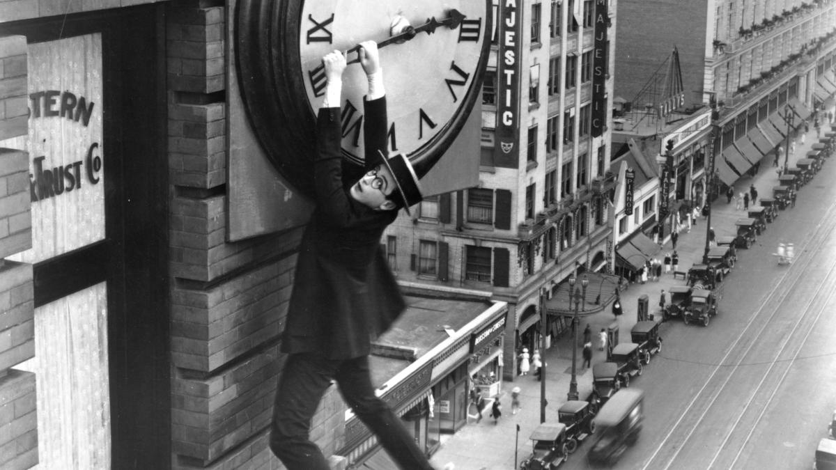 man in formal dress hanging off clock on tall building