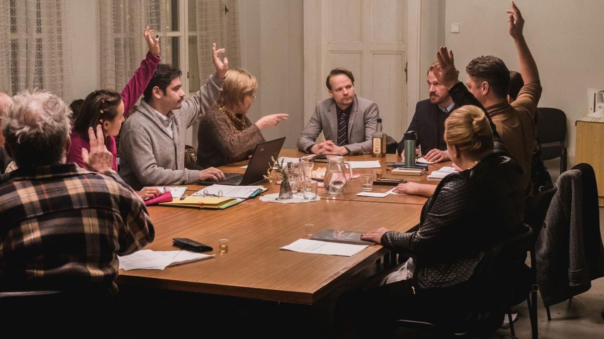 people sitting around table with notes and hands raised