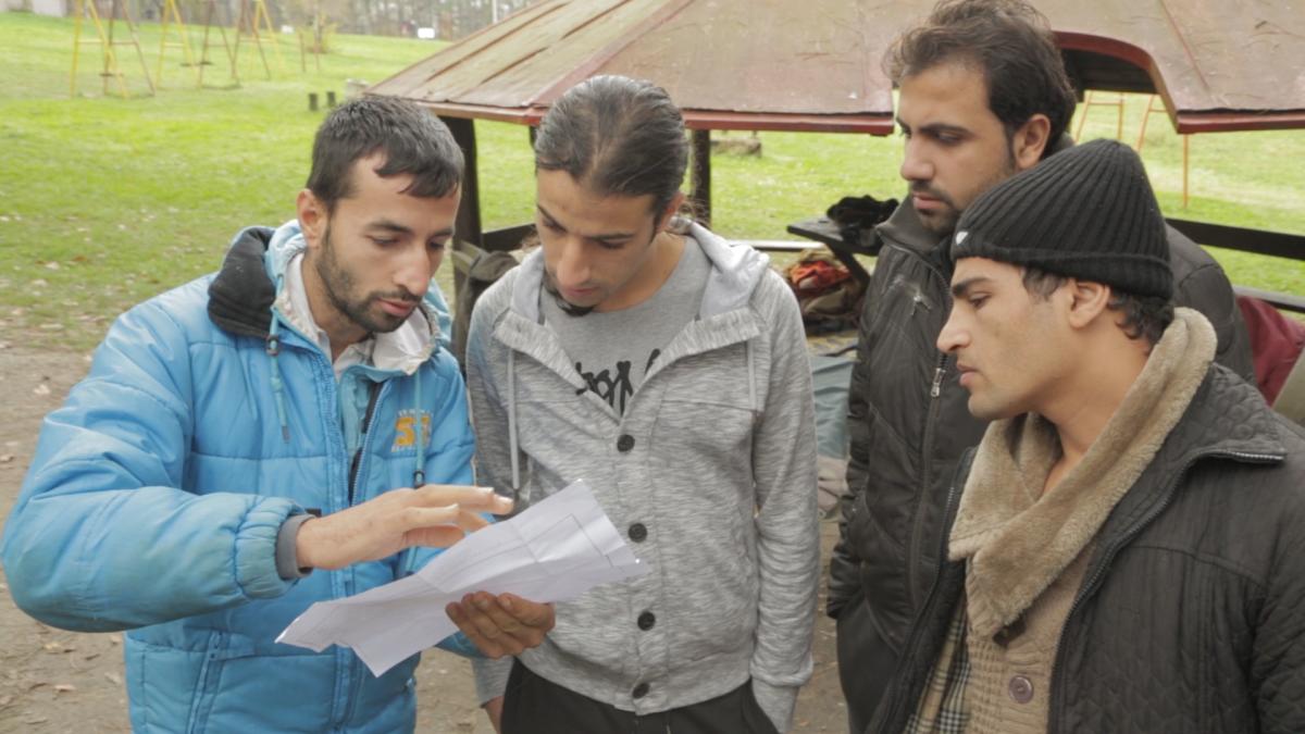 four men standing in field looking at piece of paper