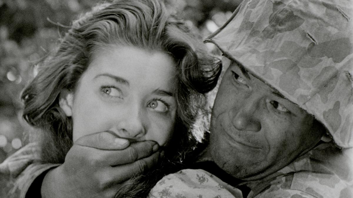 man in army uniform holding woman's mouth shut from behind