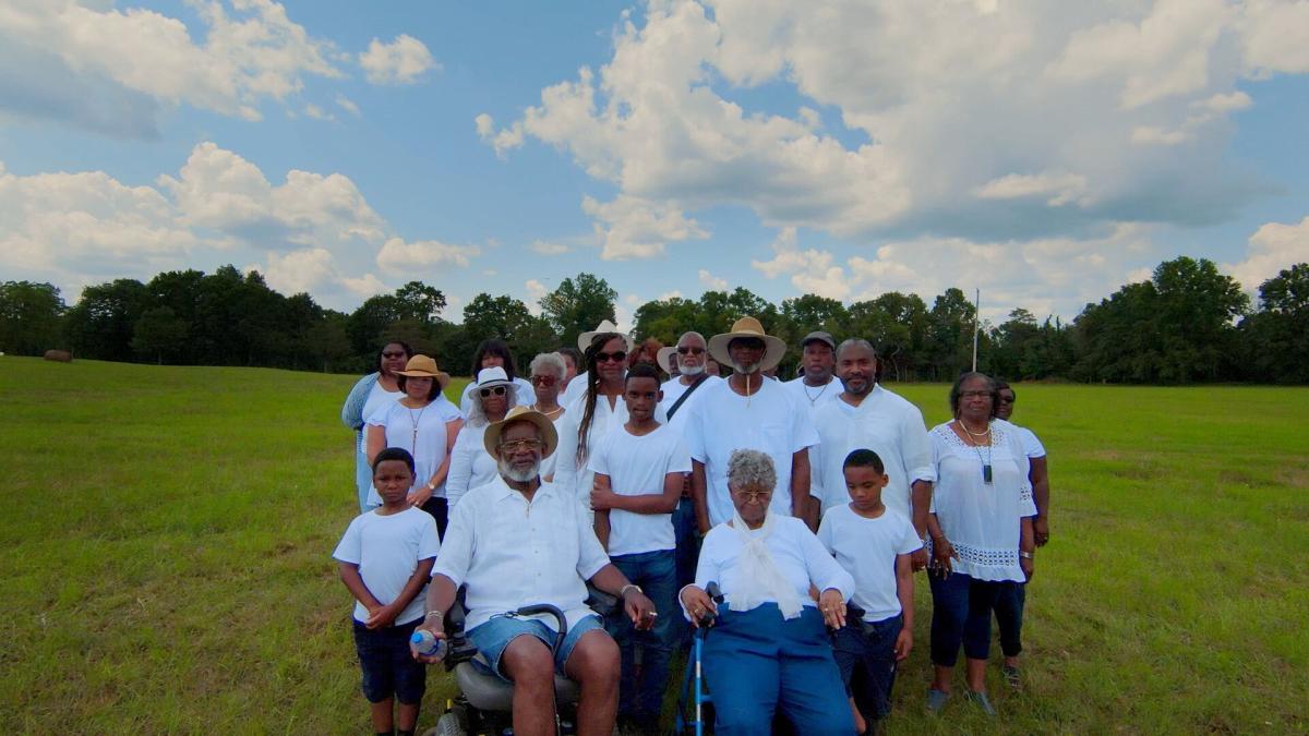large group of people posing in white shirts on green field with blue sky behind