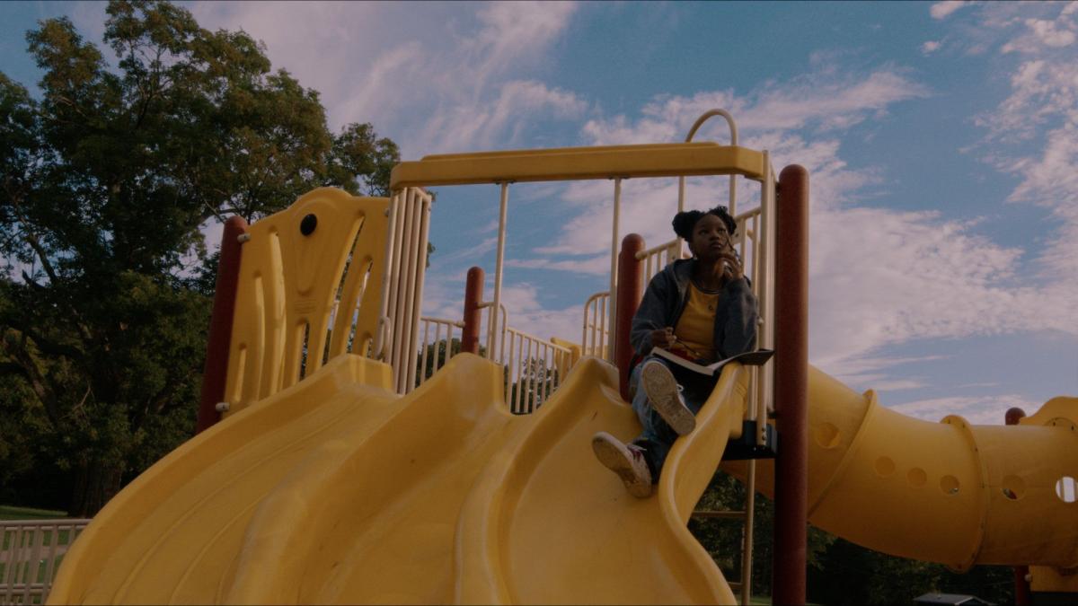 girl sitting on top of playground slide looking up into sky
