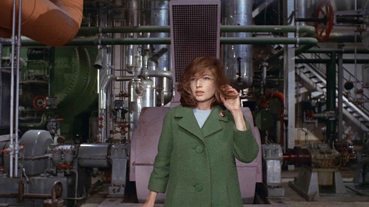 woman wearing green coat standing in front of industrial equipment