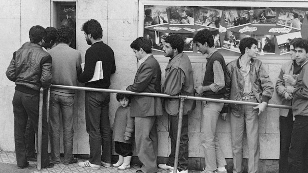 black and white photo of men and young girl standing in line outside building
