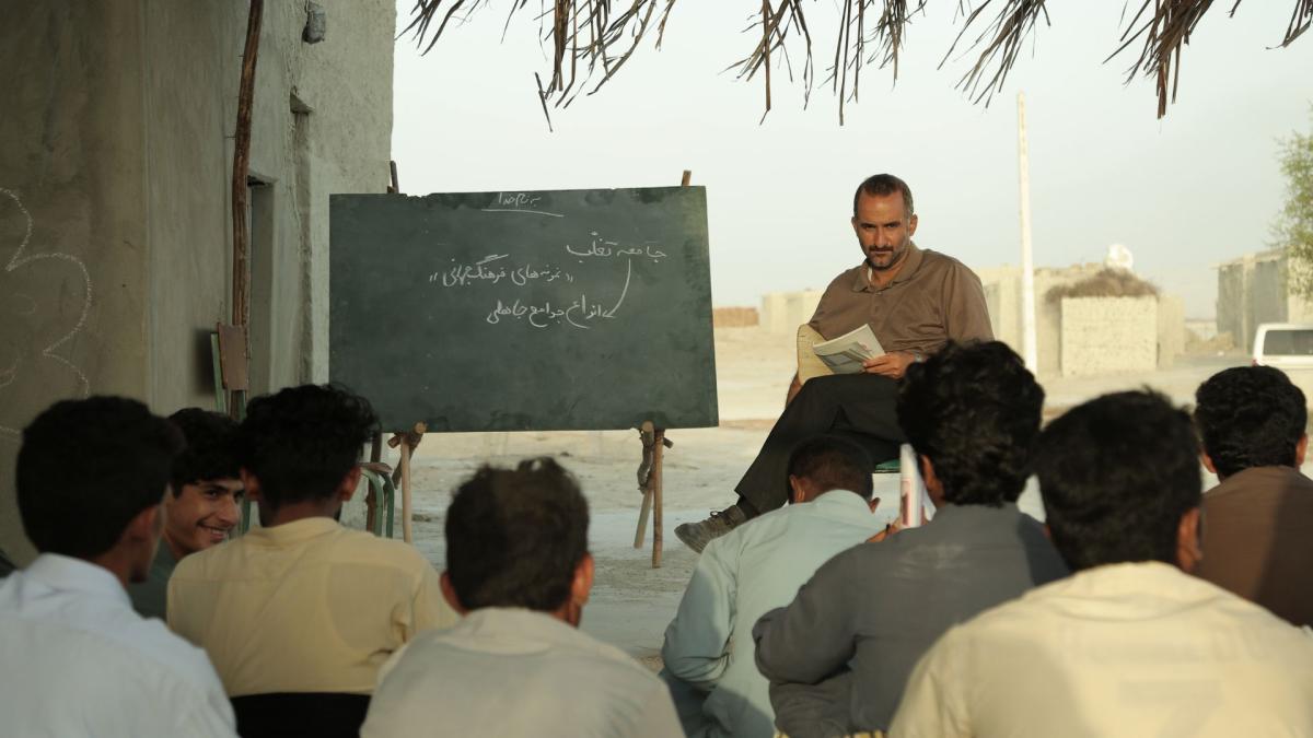 man in front of group of people outside with chalkboard next to him