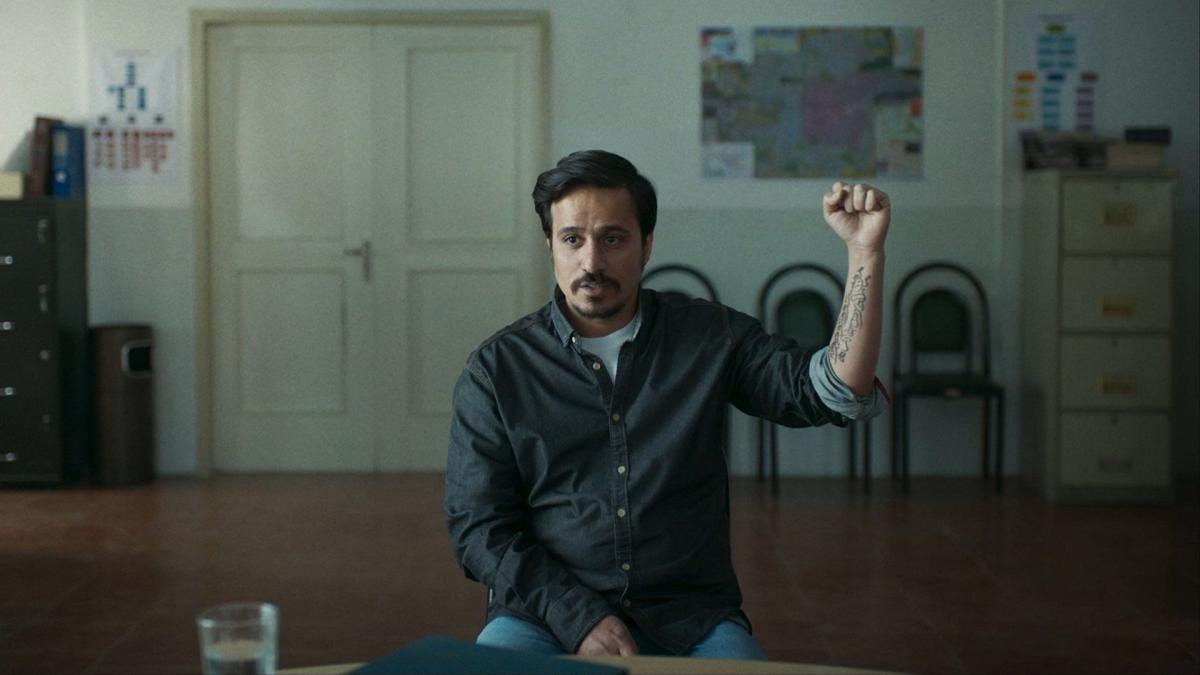 man seated in chair holding left fist up