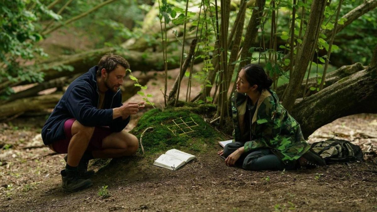 man photographing woman sitting on ground in forest