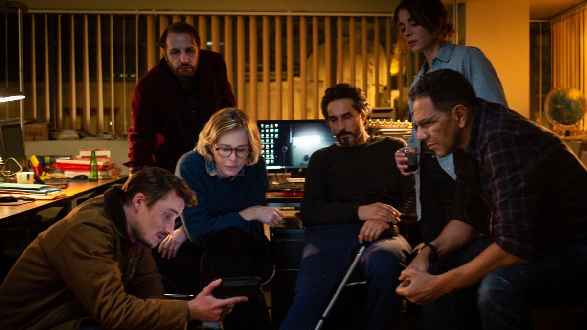 group of six people in office. gathered around phone screen leaning in