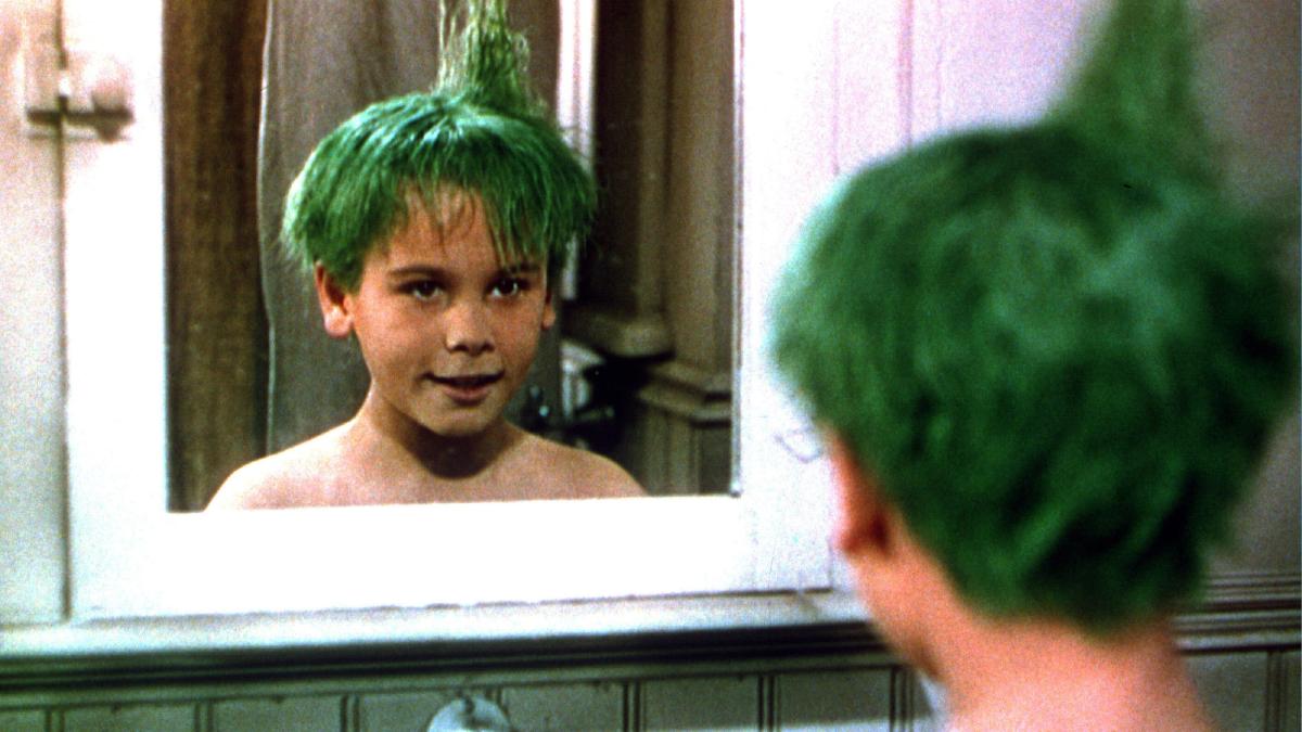 young boy with green hair looking at self in bathroom mirror
