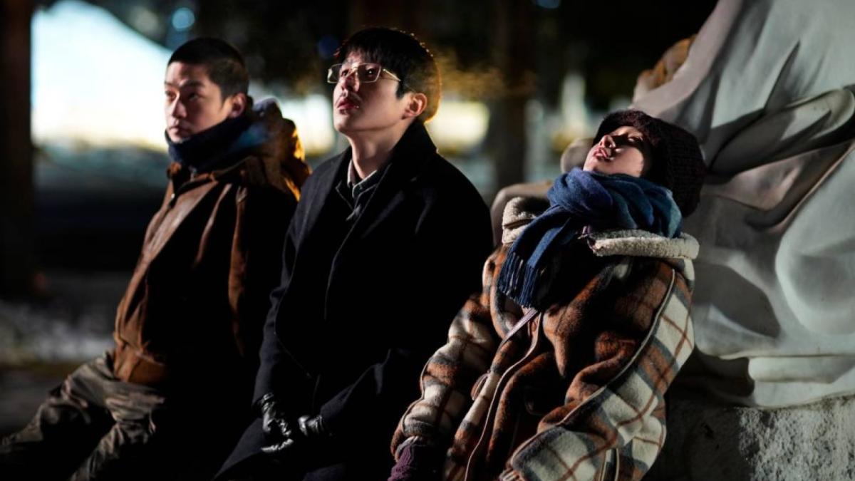 three young people sitting under bridge in winter coats