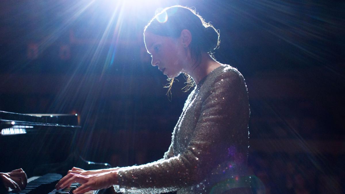 woman wearing formal dress playing the piano in front of bright spotlight