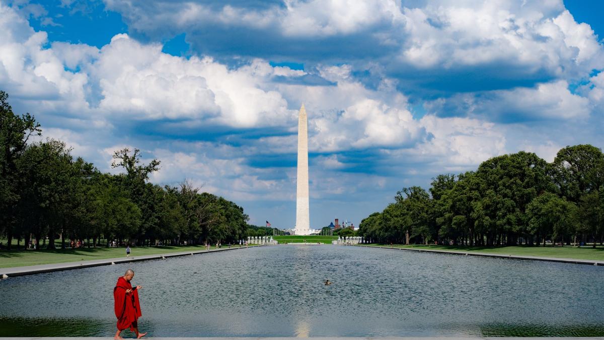monk in red robe walking across sidewalk in front of washington monument
