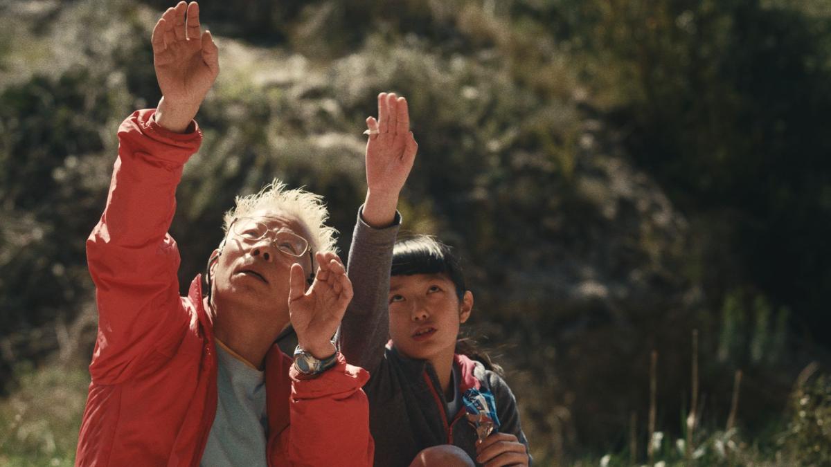 elderly man and young girl sitting outside with hands raised up and eyes to the sky