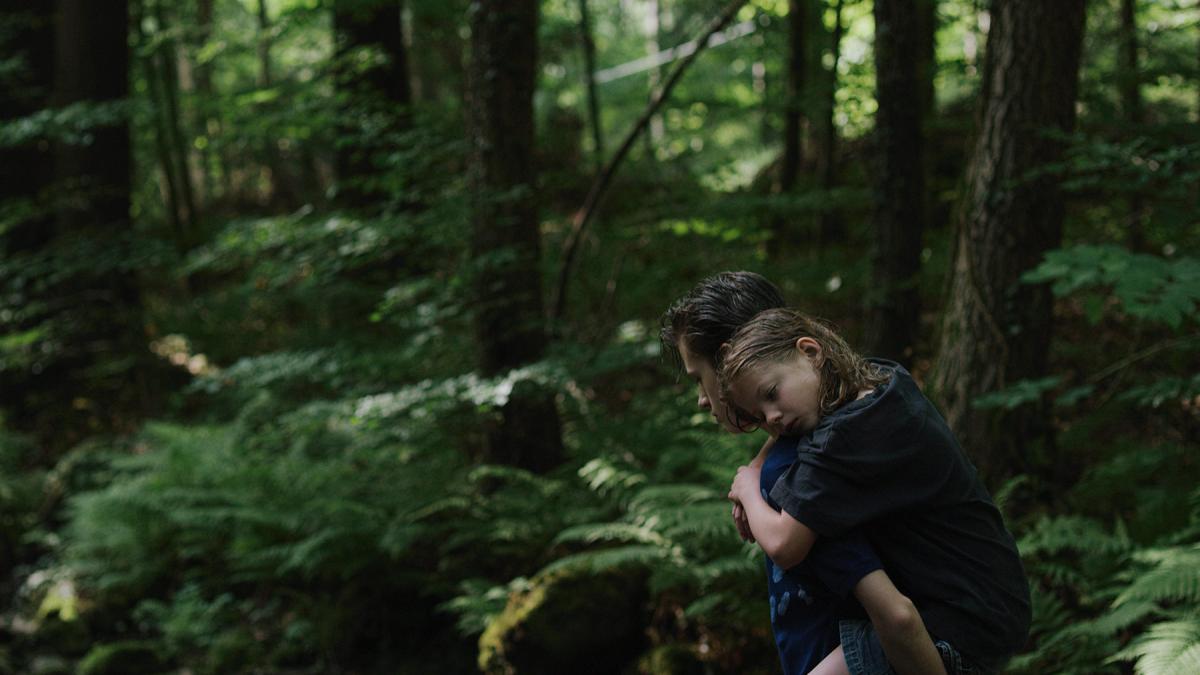 young girl being carried on man's back through wooded forest