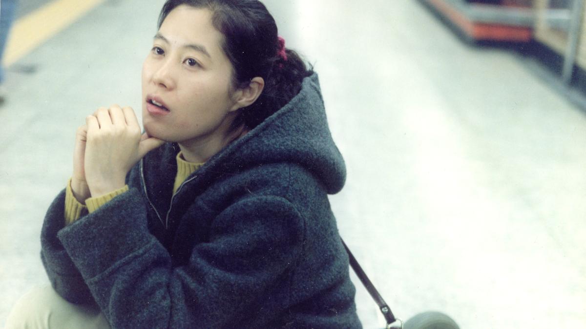 woman sitting down with hands folded in train station looking up