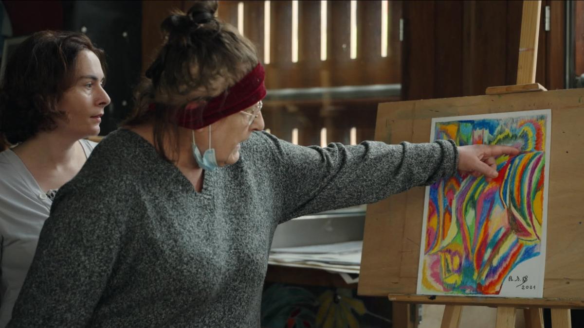 woman in studio pointing at abstract piece of art on easel