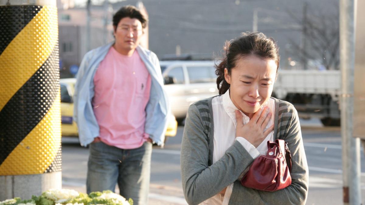 woman clutching chest and crying with man in pink shirt standing behind her looking
