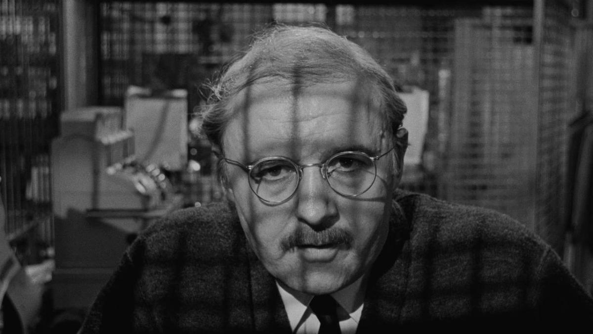 older man with glasses and suit looking through barred window