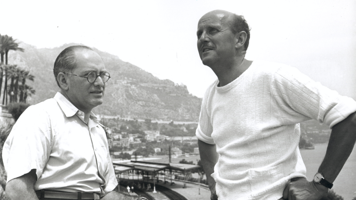 two men in white shirts standing outside with mountains behind