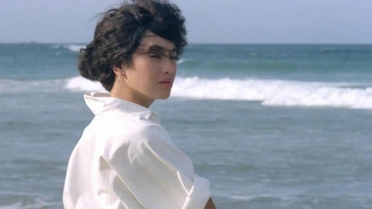 woman standing on beach wearing white shirt and turning behind her