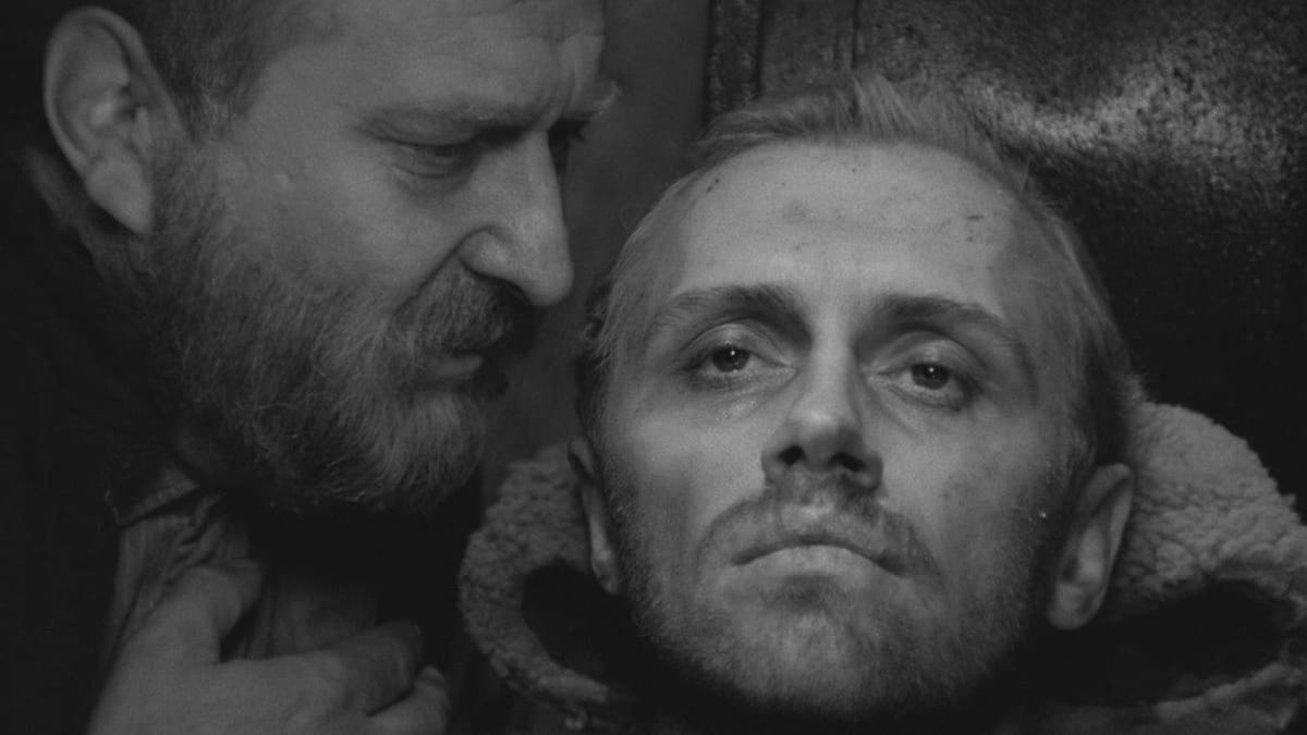 man lying down with another man leaning down to whisper in ear