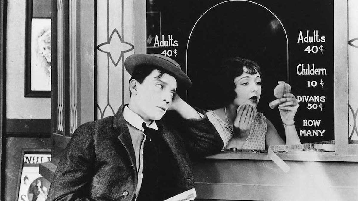 man leaning against box office window with woman seated inside