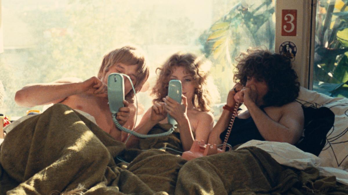 three people lying in bed in daytime on phones