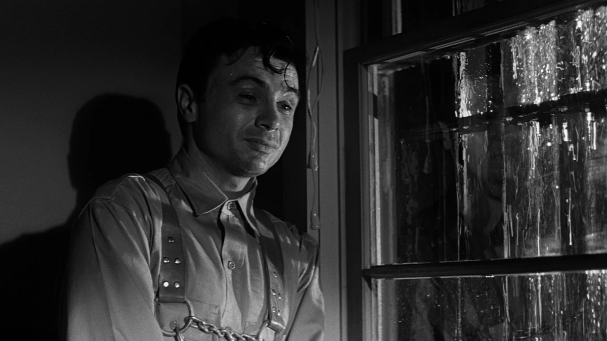 black and white image of man in jail cell near barred window