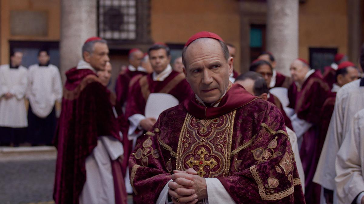 Cardinal in red robes standing in front of other cardinals
