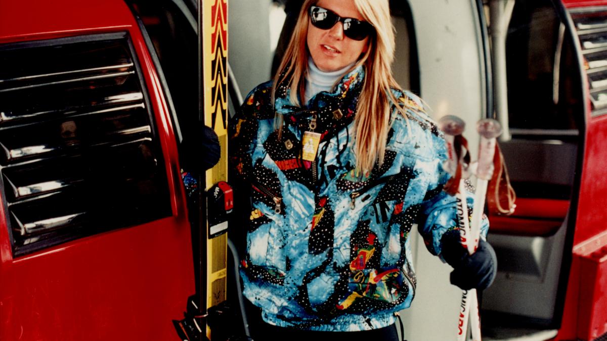 blonde woman in colorful ski jacket holding skis