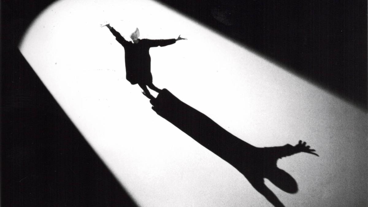 person standing on stage in spotlight with arms outstretched overhead