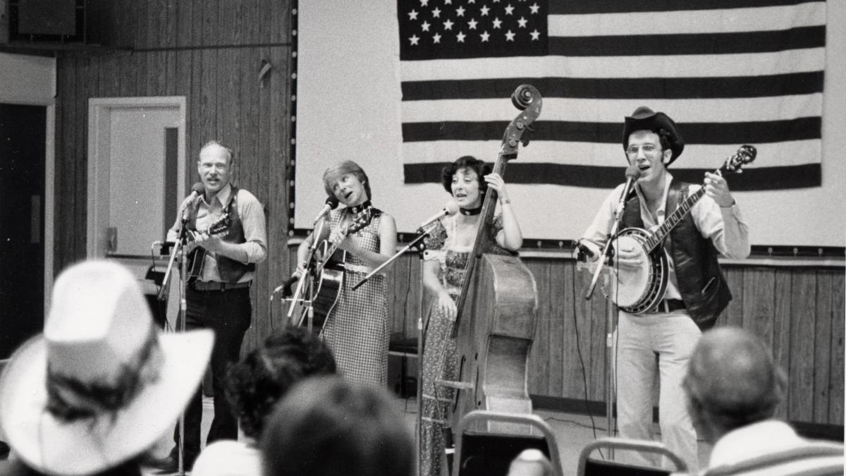 country group performing with banjos on stage with american flag behind them