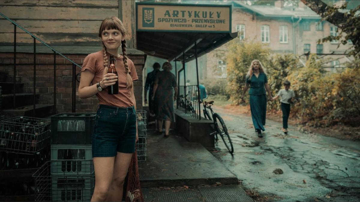 woman in shorts and braids standing at street corner holding soda