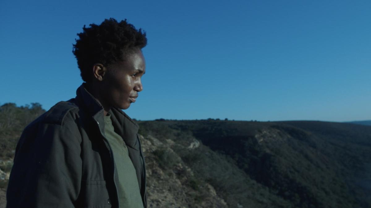 Black woman in jacket staring out over landscape with blue sky in background