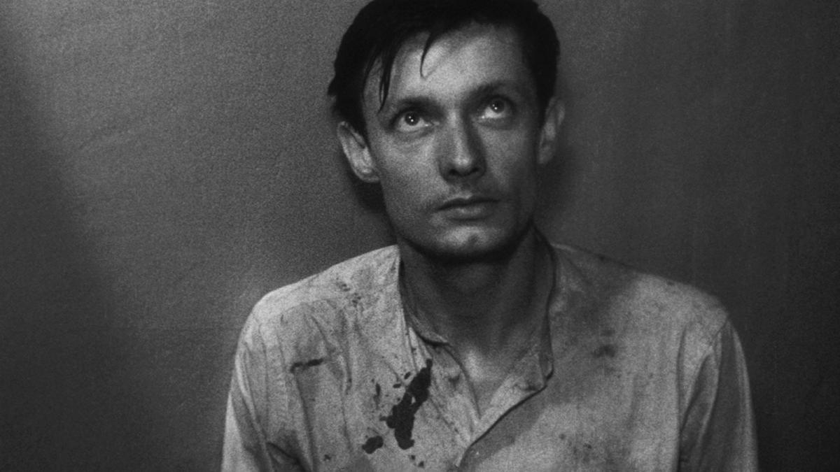 A MAN ESCAPED, 1956, black and white image of man in white button down shirt leaning against dark wall and looking upwards