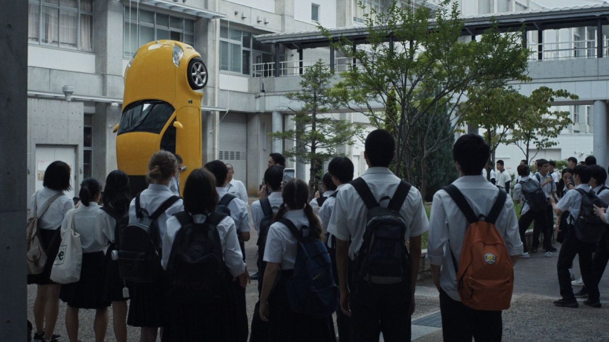 HAPPYEND, 2024, students in uniforms and backpacks standing in street looking towards yellow car turned on its side