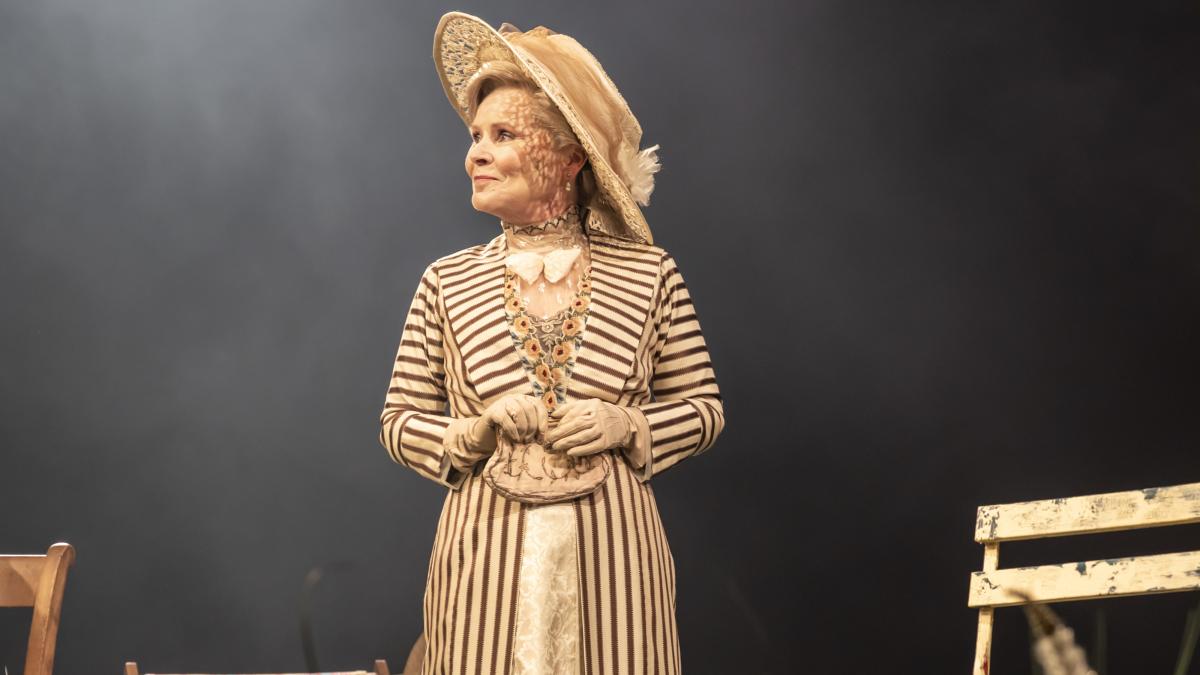 MRS. WARREN'S PROFESSION, 2025, woman standing on stage near chair wearing beige formal outfit and large hat 