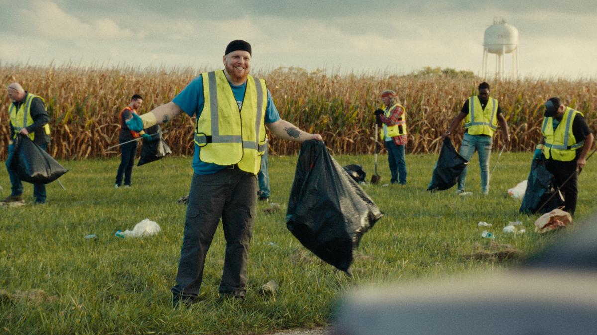 $POSITIONS, 2025, men in bright yellow vests cleaning up trash near corn field