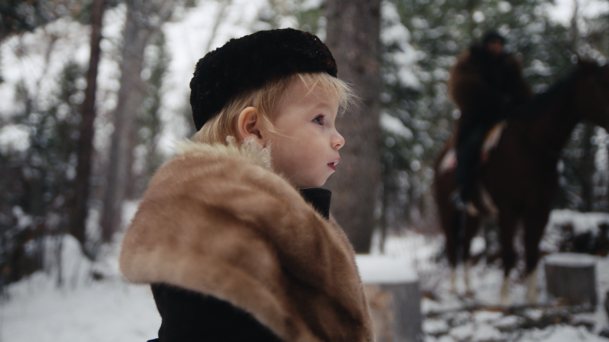 EASTERN WESTERN, 2025, small child in fur coat and cap standing in the snowy forest looking off into distance